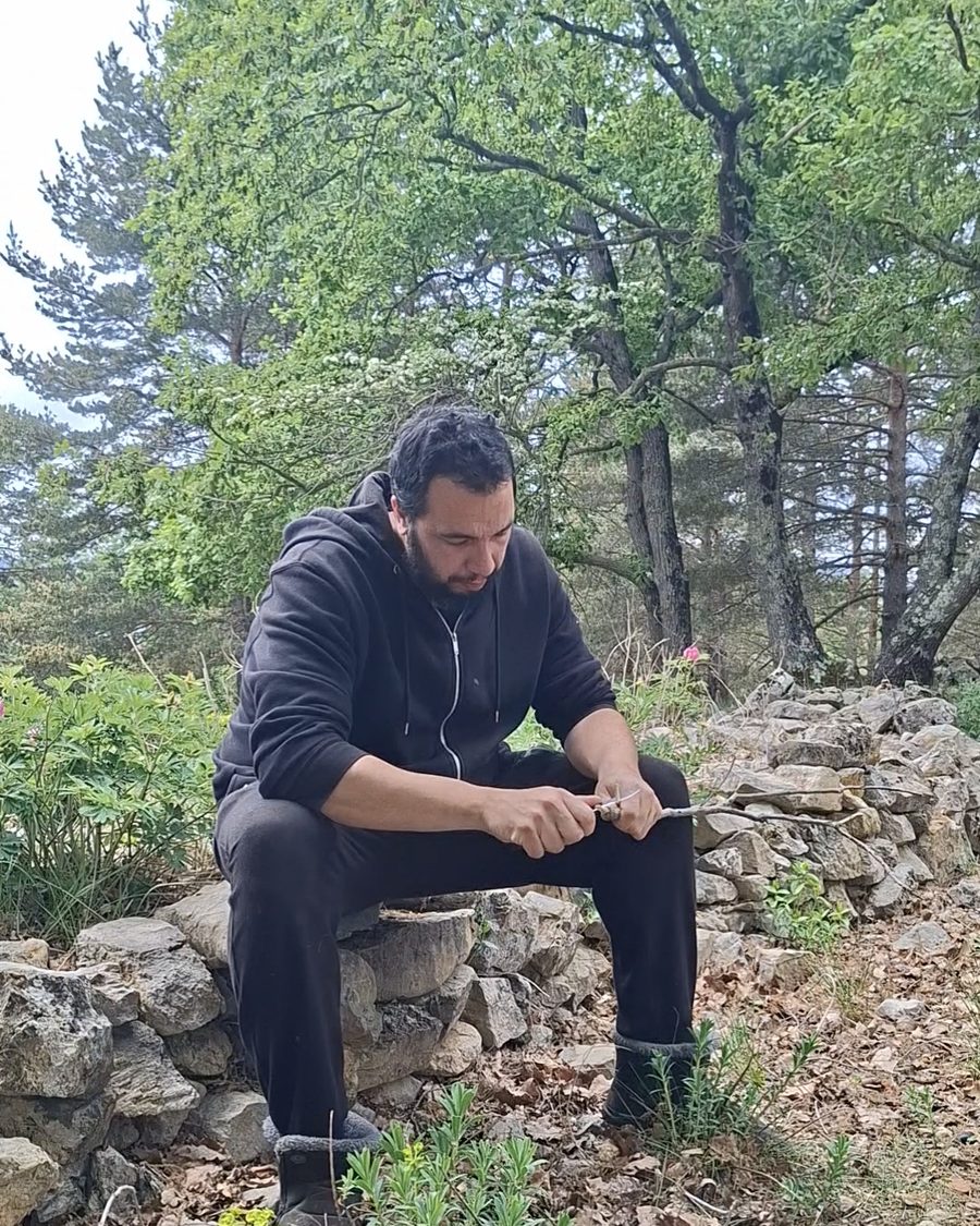 Capitán Salvaje sentado en un muro de piedra, tallando madera
